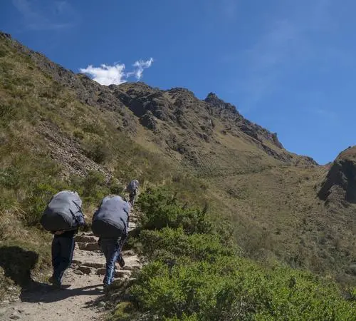 Porter carrying supplies on the classic trail with mountain peaks visible in the distance